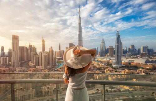 Woman with a white hat is standing on a balcony in front of the skyline from Dubai