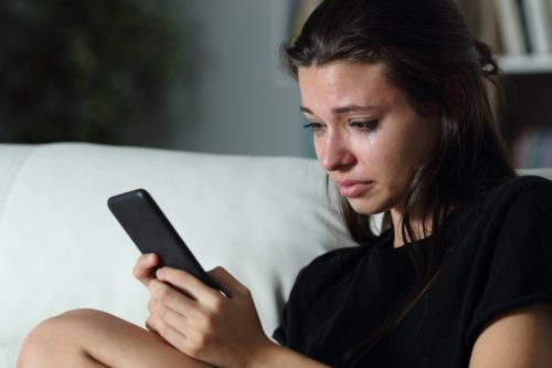 Woman looking at her phone with tears streaming down her face. 