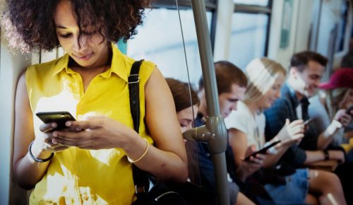 Woman on her phone on the bus in a bright yellow top. 