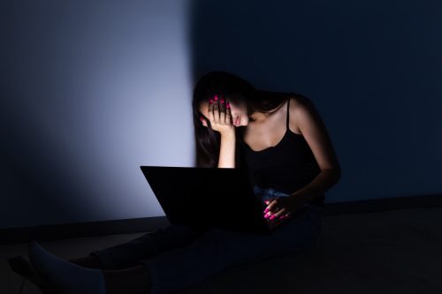 Women with bright peonk nails looking at her lptop in distress. 
