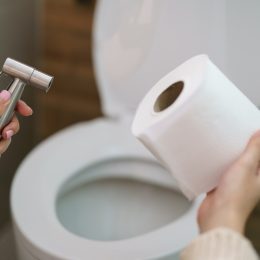 woman holding bidet sprayer and roll of toilet paper