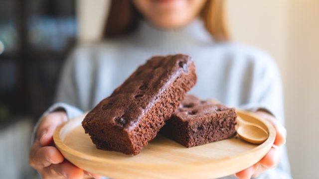 A closeup of brownies on a plate behind held out by a young woman