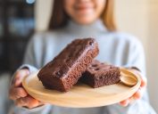 A closeup of brownies on a plate behind held out by a young woman
