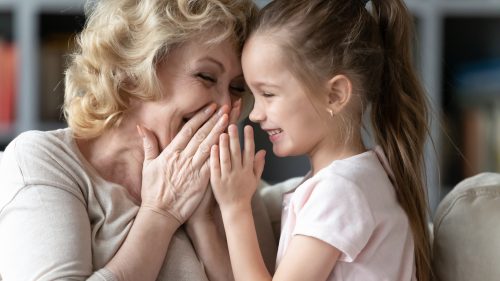 grandmother whispering a joke to her granddaughter