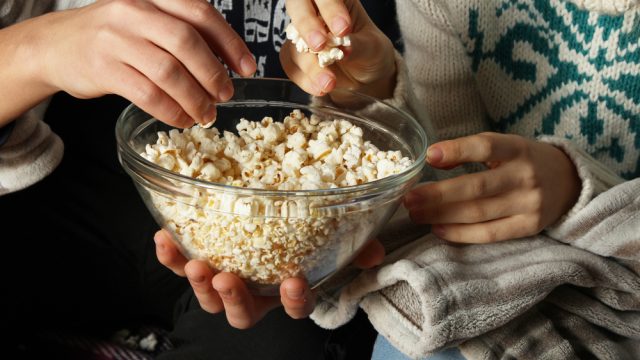 A closeup of two people eating popcorn out of a glass bowl