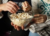 A closeup of two people eating popcorn out of a glass bowl