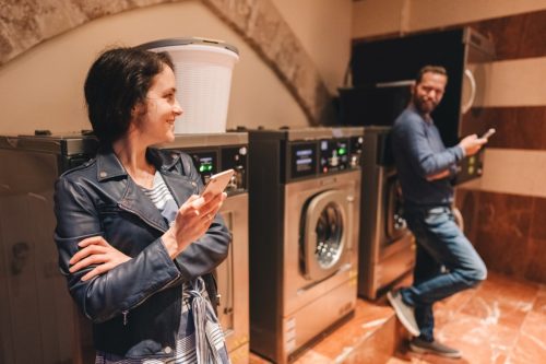 Young people using smartphones while washing clothes in public laundrette