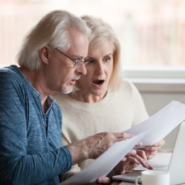 A senior couple looking at a letter with a shocked expression on their faces