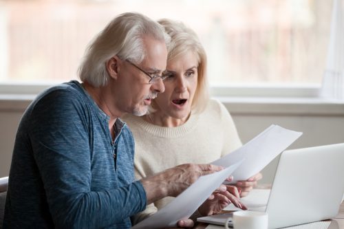 A senior couple looking at a letter with a shocked expression on their faces