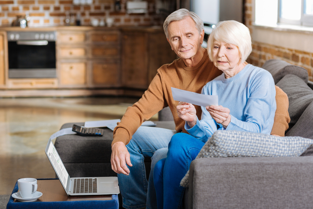 A senior couple sitting on the couch and opening and envelope