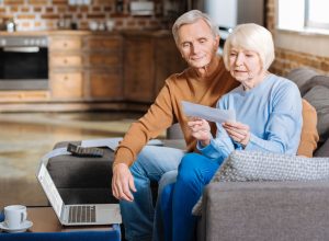 A senior couple sitting on the couch and opening and envelope