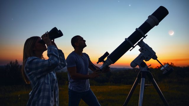 A couple using binoculars and a telescope to stargaze