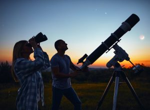 A couple using binoculars and a telescope to stargaze