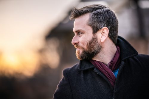 Profile shot of a bearded man wearing a peacoat and scarf outside.