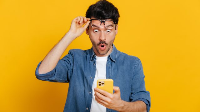 man looking shocked as he reads dirty jokes off his phone