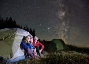 A family camping in a tent while looking up at the Milky Way and night sky