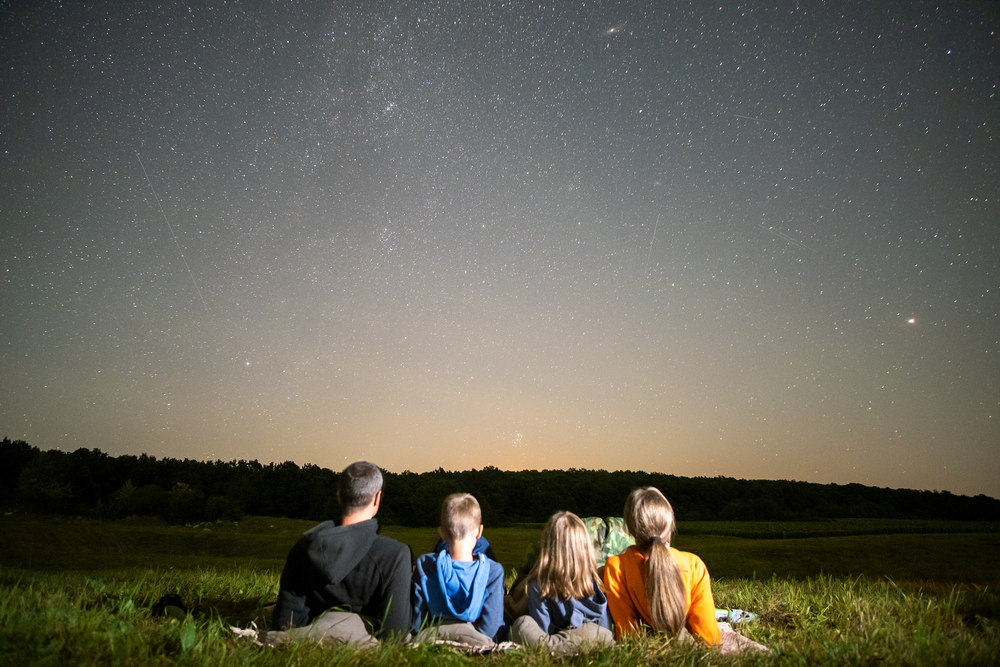 A family of four sitting in a field and stargazing