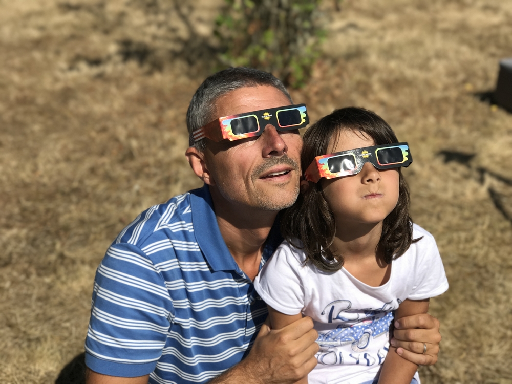 A daughter and father looking up at a solar eclipse with special viewing glasses