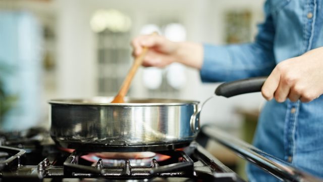 Close-up midsection image of woman cooking food in frying pan. Utensil is placed on gas stove. Female is stirring food in cooking pan. She is preparing food in domestic kitchen.