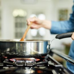 Close-up midsection image of woman cooking food in frying pan. Utensil is placed on gas stove. Female is stirring food in cooking pan. She is preparing food in domestic kitchen.