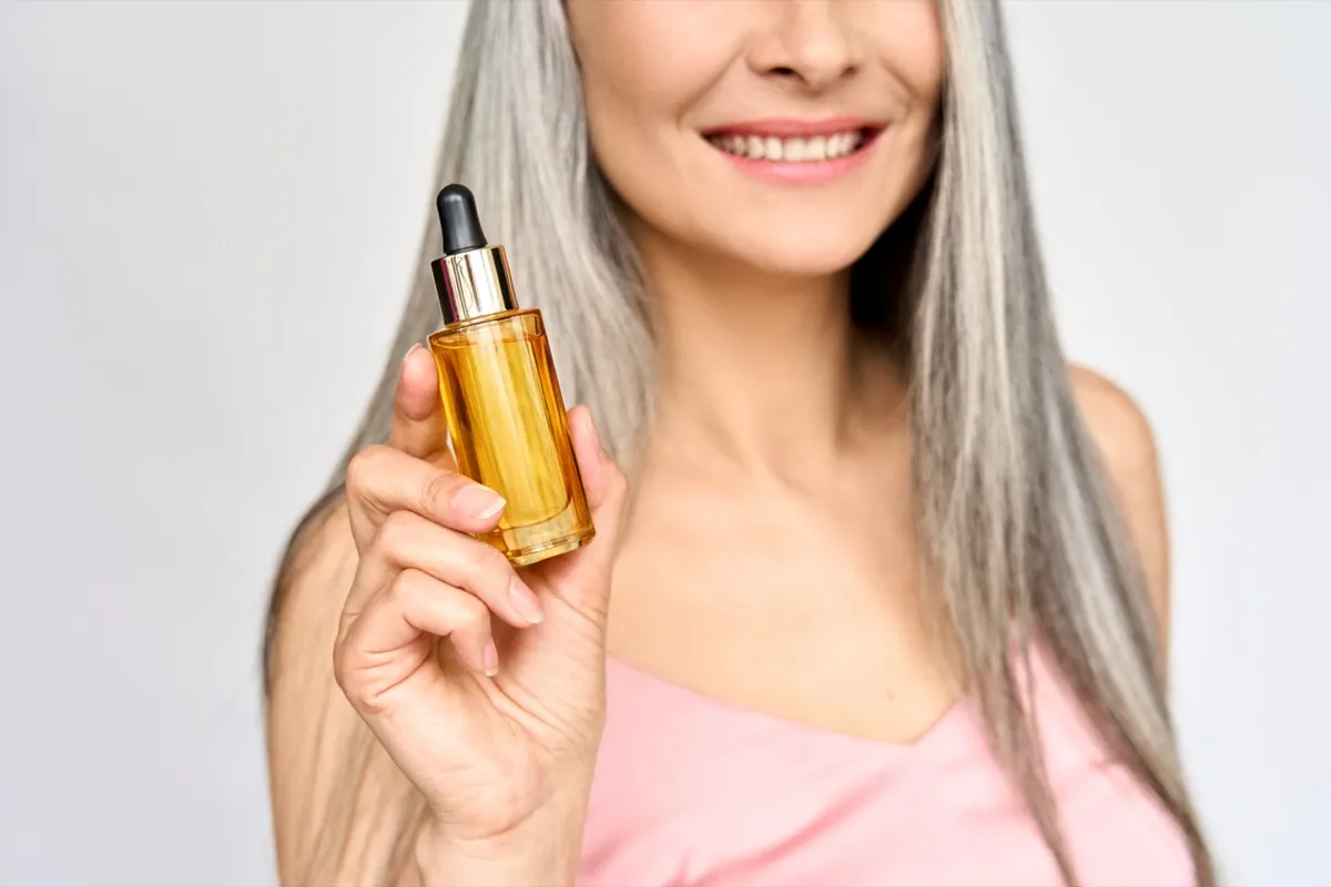 Asian woman with grey hair holding bottle of oil
