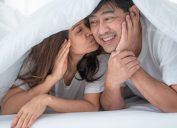 cặp đôi mỉm cười trên giường dưới tấm chăn