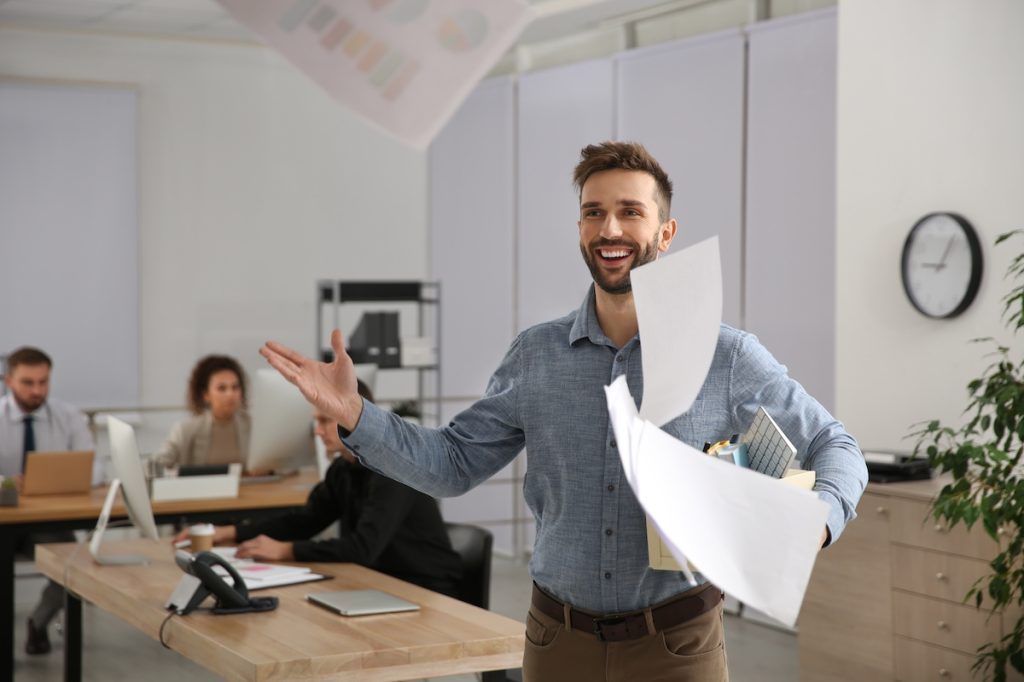 Man quitting his office job, smiling and tossing papers in the air