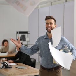 A happy young man who just quit his job throwing papers in the air.
