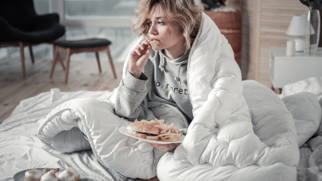 Woman wrapped in a blanket and eating junk food.