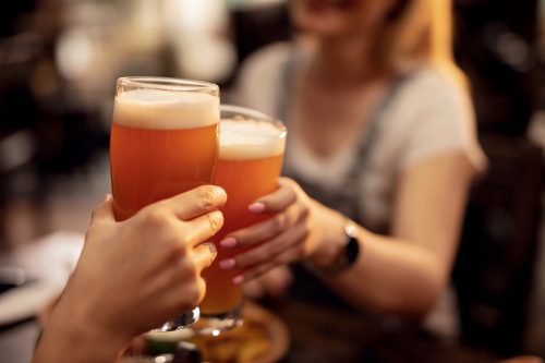 Two people toasting with glass mugs of beer.