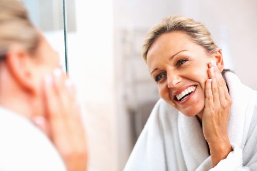 Older woman smiling at herself in the mirror.