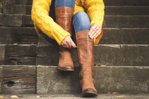 Woman sitting on stairs and fasten zipper on her leather boots. 