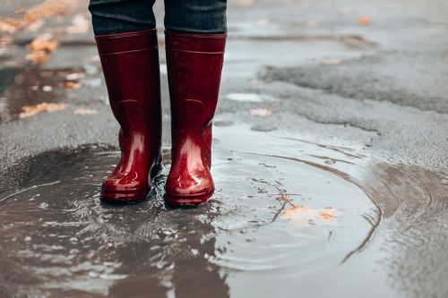 Woman with dark red rubber boots jumping in puddle