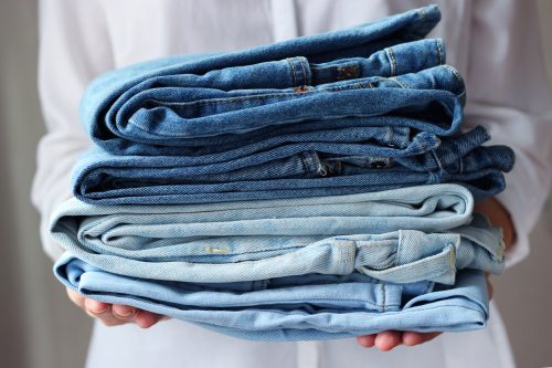 Person holding a stack of folded jeans.