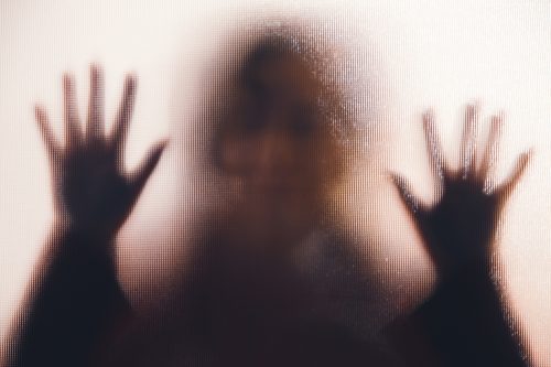 Silhouette of a woman with her hand pressed against a glass window.