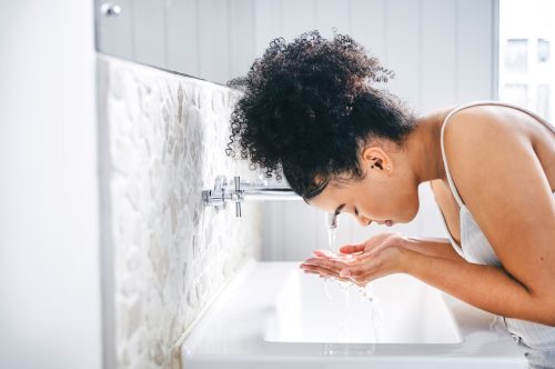 Woman washing her face in the bathroom sink.
