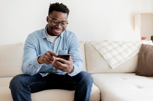 Man sitting on couch and smiling at cell phone