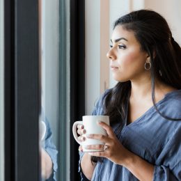 Woman standing alone at a window with a mug.