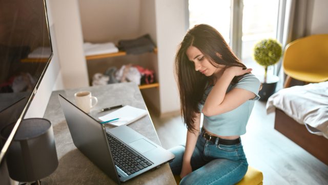 Woman sitting with laptop rubbing her shoulder.