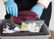 Gloved hands of an airport security person examining the contents of a bin with a traveler's belongings.