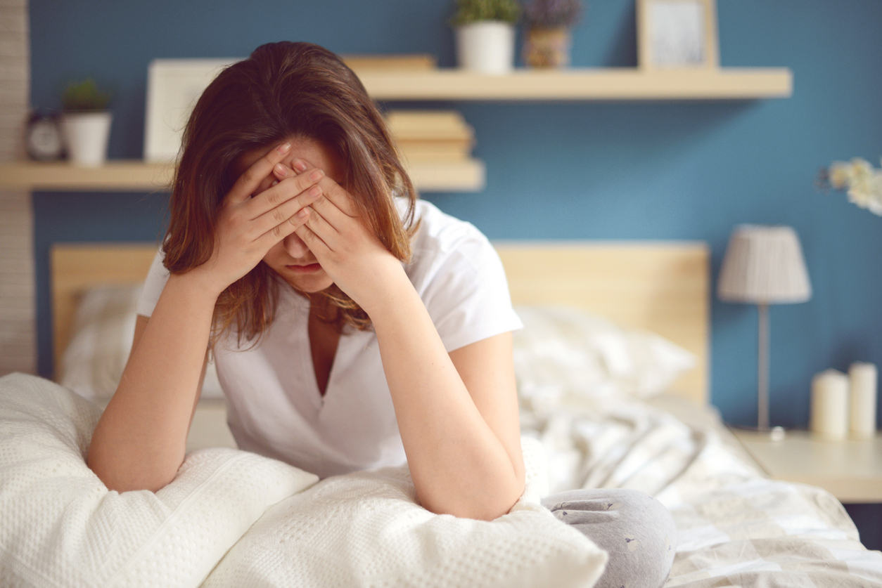 Woman sitting up in bed feeling sick with a headache. 