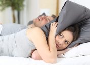 Man snoring while his wife is covering ears with the pillow.