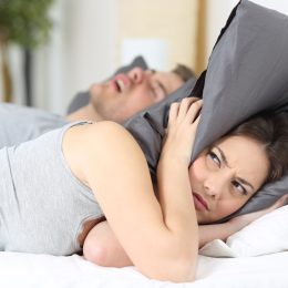 Man snoring while his wife is covering ears with the pillow.