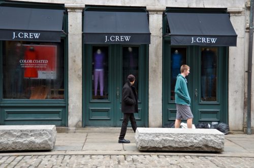 an abandoned j crew store front with passerby walking in front