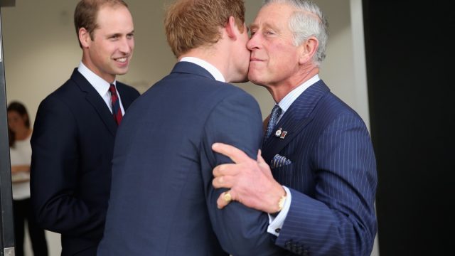 King Charles kissing Prince Harry on cheek with Prince William standing behind.