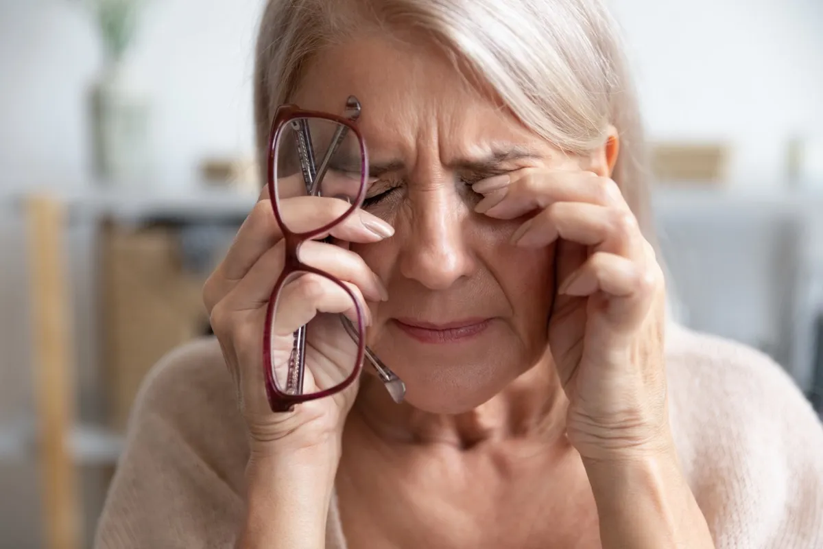 close up of older woman rubbing eyes holding glasses