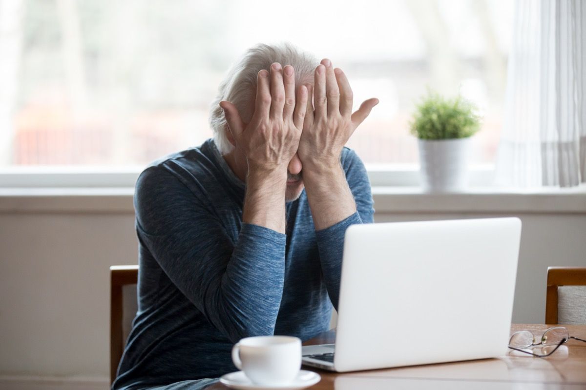 Fatigued senior mature man sitting in front of laptop holding his hands to his eyes