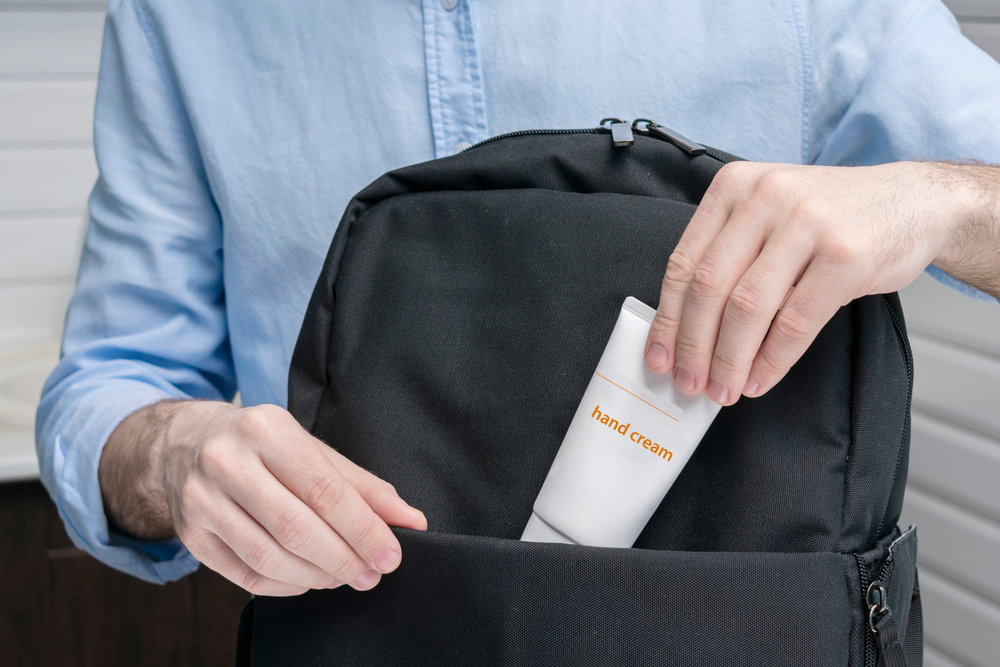 Close up of a man placing a bottle of hand cream in his carry on bag