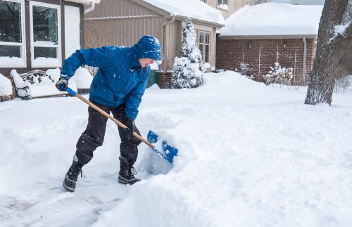 Man in winter coat shoveling snow in yard