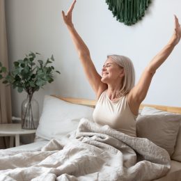 A mature woman looking happy and stretching in bed.